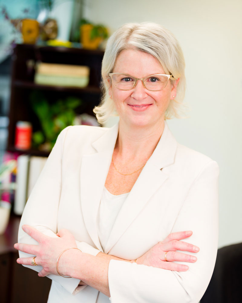 Professional headshot of Fern Sabo, Principal and Managing Director of Spring Creative Inc., wearing a white blazer and gold glasses, representing strategic digital leadership in the West Kootenays.